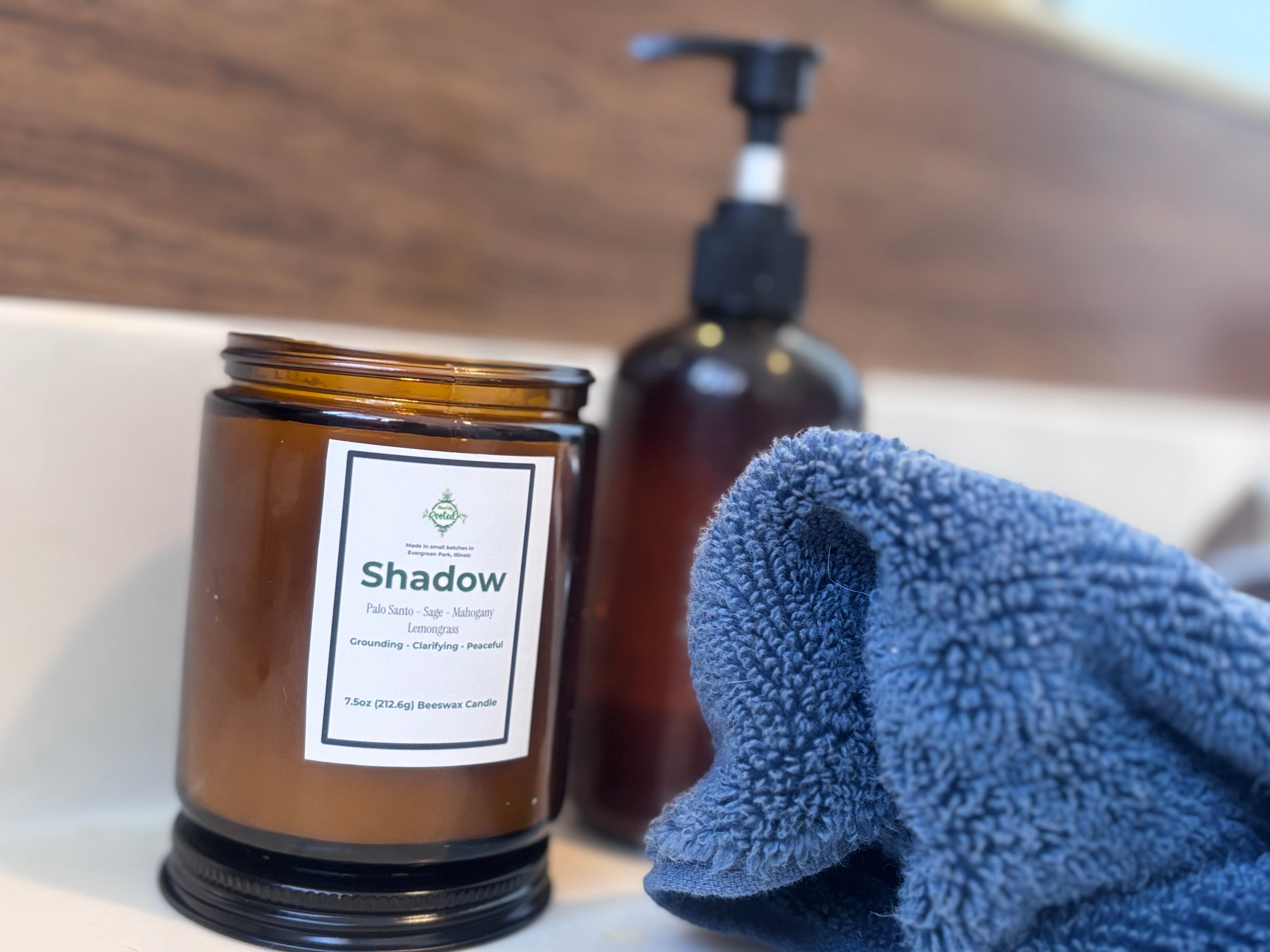 Brown candle labeled 'Shadow' with a blue towel and pump bottle on a wooden surface.