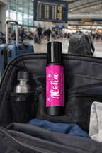 Pink bottle labeled 'Aloha' in a suitcase with people and luggage in the background