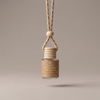 A glass car diffuser bottle with a beige label reading 'Warm Apple Cider Donuts' and a natural wood hanging collar with a braided cord, centered against a warm taupe background.