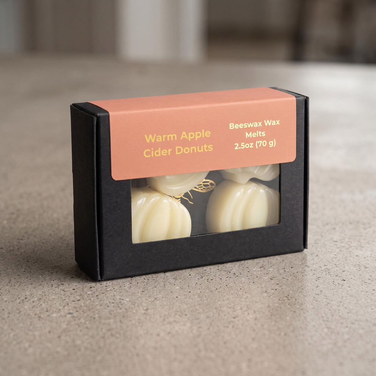 A black rectangular box of beeswax melts with a peach-colored label reading 'Warm Apple Cider Donuts' and 'Beeswax Wax Melts 2.5oz (70 g)'.