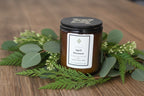 Candle jar labeled 'April Showers' with greenery on a wooden surface