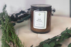Candle labeled 'April Showers' on a white surface with greenery