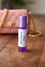 Roll-on bottle labeled 'Blackberry Bliss' on a wooden surface with a pink handbag in the background.