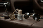 Small bottle with wooden top labeled 'Distinguished Gentleman' on a leather dash next to watch and aviator sunglasses.  Masculine lifestyle photograph with a nostalgic aesthetic.