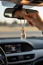 Small bottle with wooden top labeled 'Distinguished Gentleman' being hung from the rear view mirror of a car by a masculine hand.  