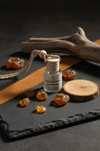 Small bottle labeled 'Distinguished Gentleman' on a slate surface with suede, hickory wood, driftwood and amber.