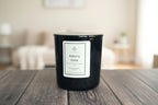 Black vessel candle on wooden surface with living room backgorund.