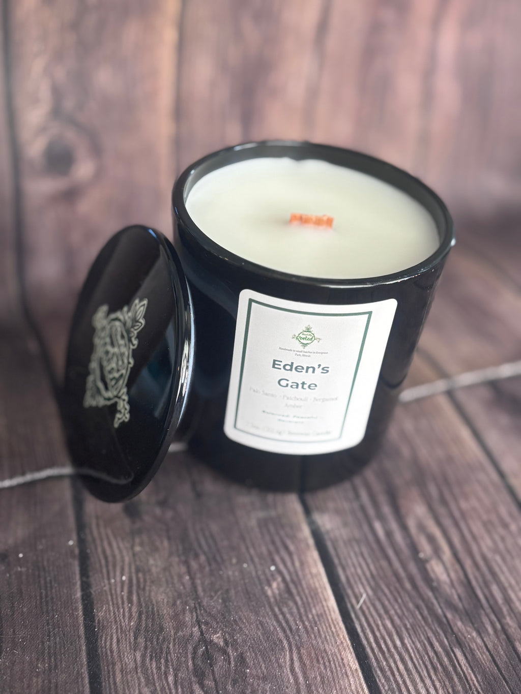 Black vessel candle with Eden's Gate label on wooden surface with wooden wick.