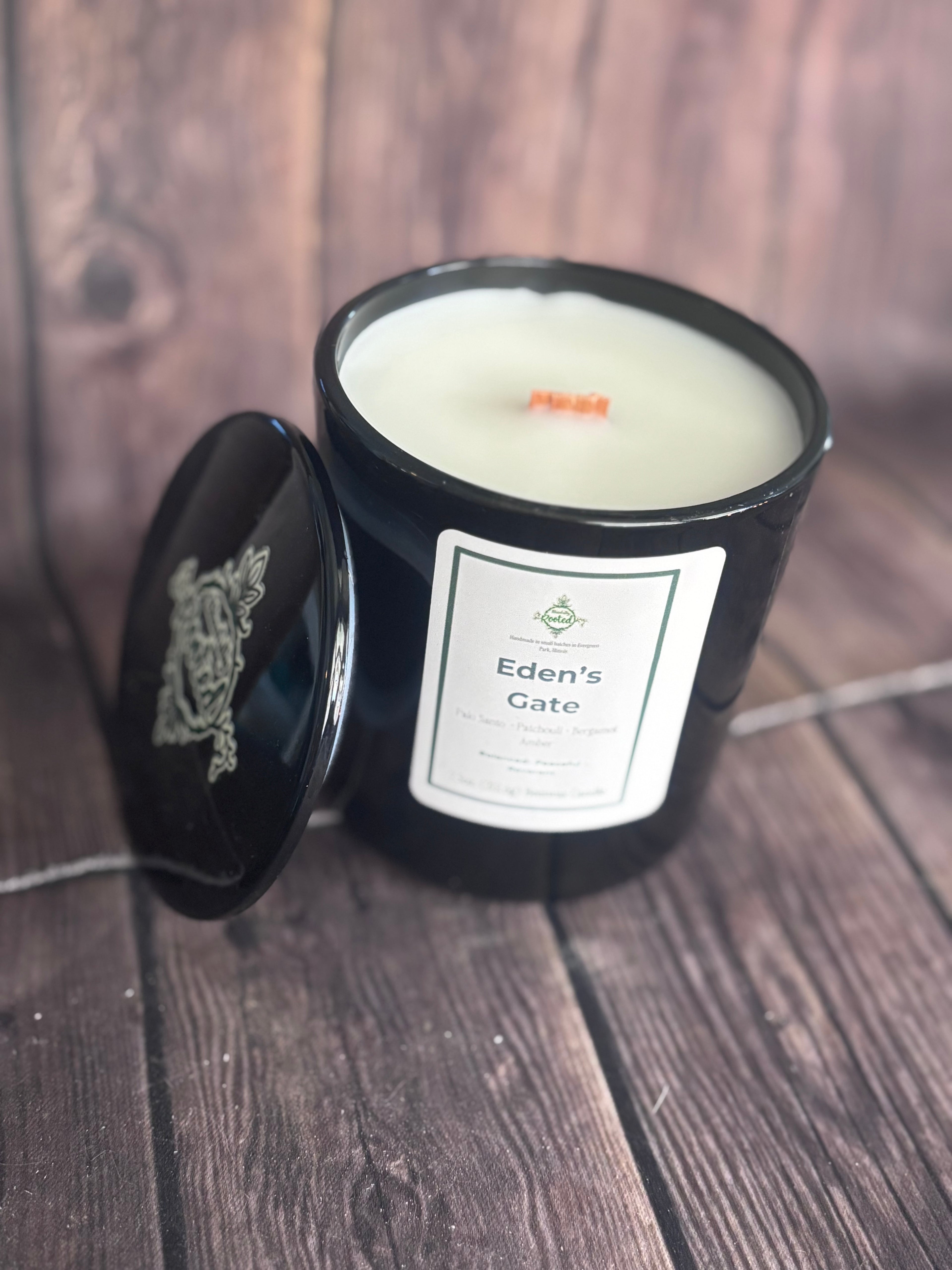 Black vessel candle with Eden's Gate label on wooden surface with wooden wick.