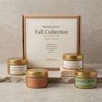 Blissfully Rested Fall Collection Discovery Box set with four beeswax candles in gold-lidded jars arranged in front of a kraft paper box on a stone surface.