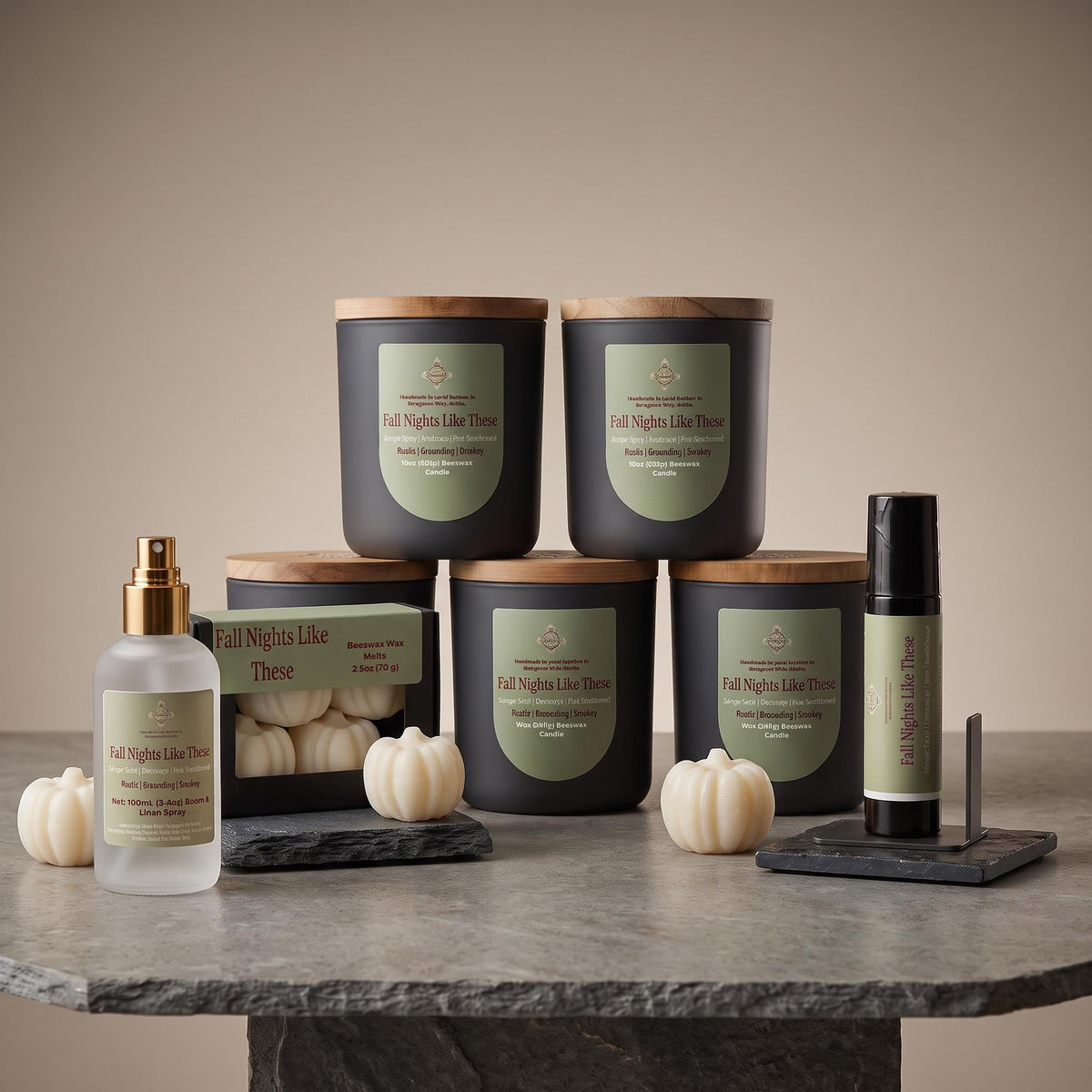 A curated collection of fall-themed home fragrance products from The Fragrance Company, including four scented candles in matte black jars with bamboo lids, a body mist in a frosted bottle with a gold sprayer, and a rollerball, all arranged on a gray stone table with small white pumpkins against a warm beige background.