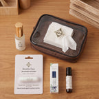 A curated wellness gift set arranged on a light wood tabletop, including a brown translucent zip case with white tissue paper, a small bottle with a gold cap labeled Deep Sleep, a Breathe Easy aromatic inhaler card, a lavender eucalyptus roller bottle, and a small amber bottle.