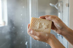 Bar of soap with honeycomb and bee design in wet soapy hands with a shower in the background.