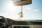 Small bottle labeled 'Hope of Morning' with a strap hanging from a car with sunlight in the background