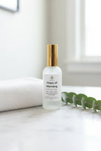 Frosted bottle labeled 'Hope of Morning' on a bathroom counter near clean linens, as crisp and fresh as the new towel on the counter.  