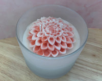 Detail picture of the sculpted pink flower on top of the candle in a frosted vessel. 
