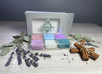 Set of colorful wax melts in a decorative box with lavender and cinnamon sticks on a wooden surface.