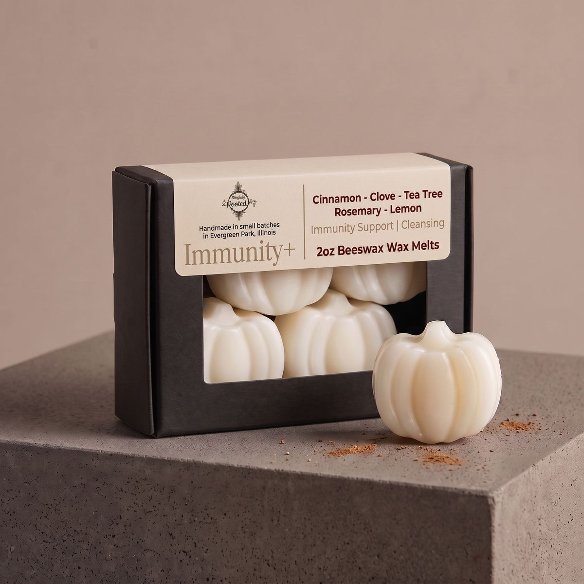 A boxed set of pumpkin-shaped beeswax melts sits on a gray stone pedestal against a warm beige background. The black-and-cream box reads 'Immunity+' and lists scents including cinnamon, clove, tea tree, rosemary, and lemon.