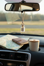 Last One Standing car diffuser hanging from a rear view mirror with a road trip notebook and coffee on the dash of a black car interior. 
