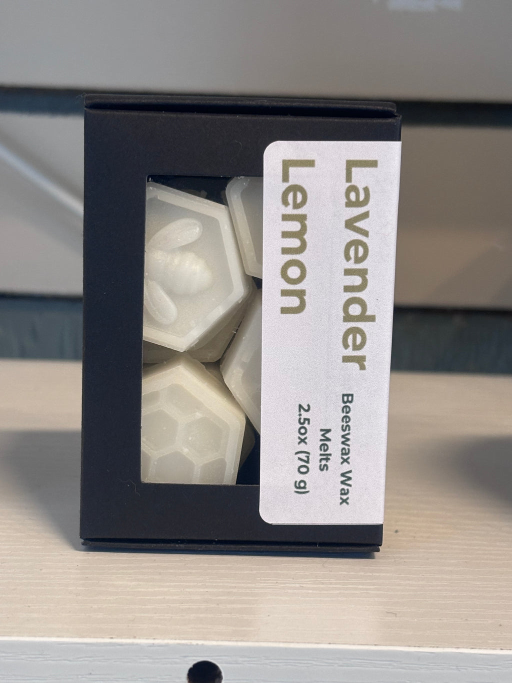 A black box of Lavender Lemon beeswax melts with a clear window showing the white hexagonal wax melts inside, set on a light wood surface.