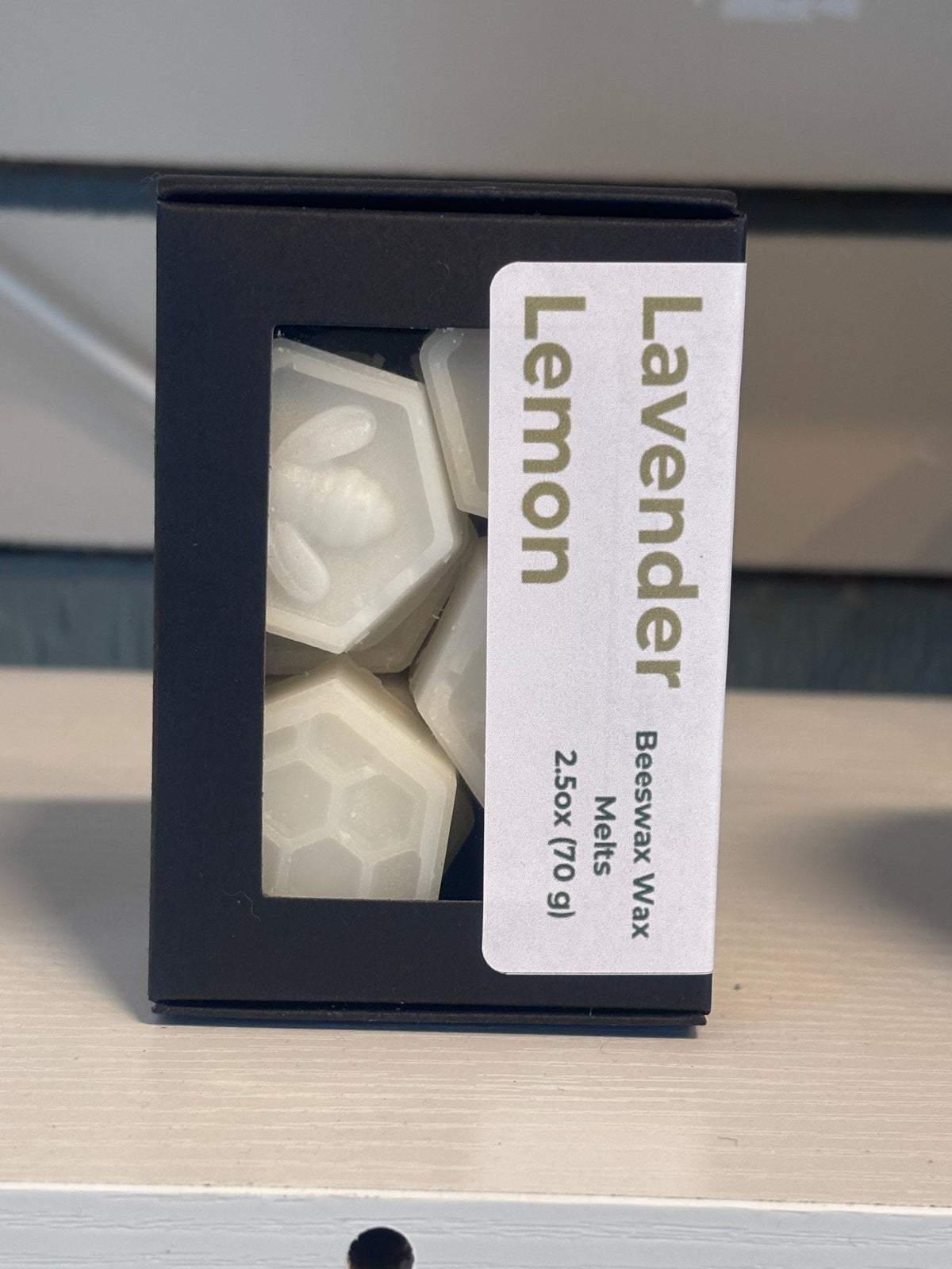 A black box of Lavender Lemon beeswax melts with a clear window showing the white hexagonal wax melts inside, set on a light wood surface.