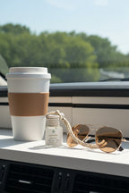 Small glass diffuser bottle labeled 'Lavender Lemon' with a jute cord on a dashboard with a cup of coffee and sunglasses.