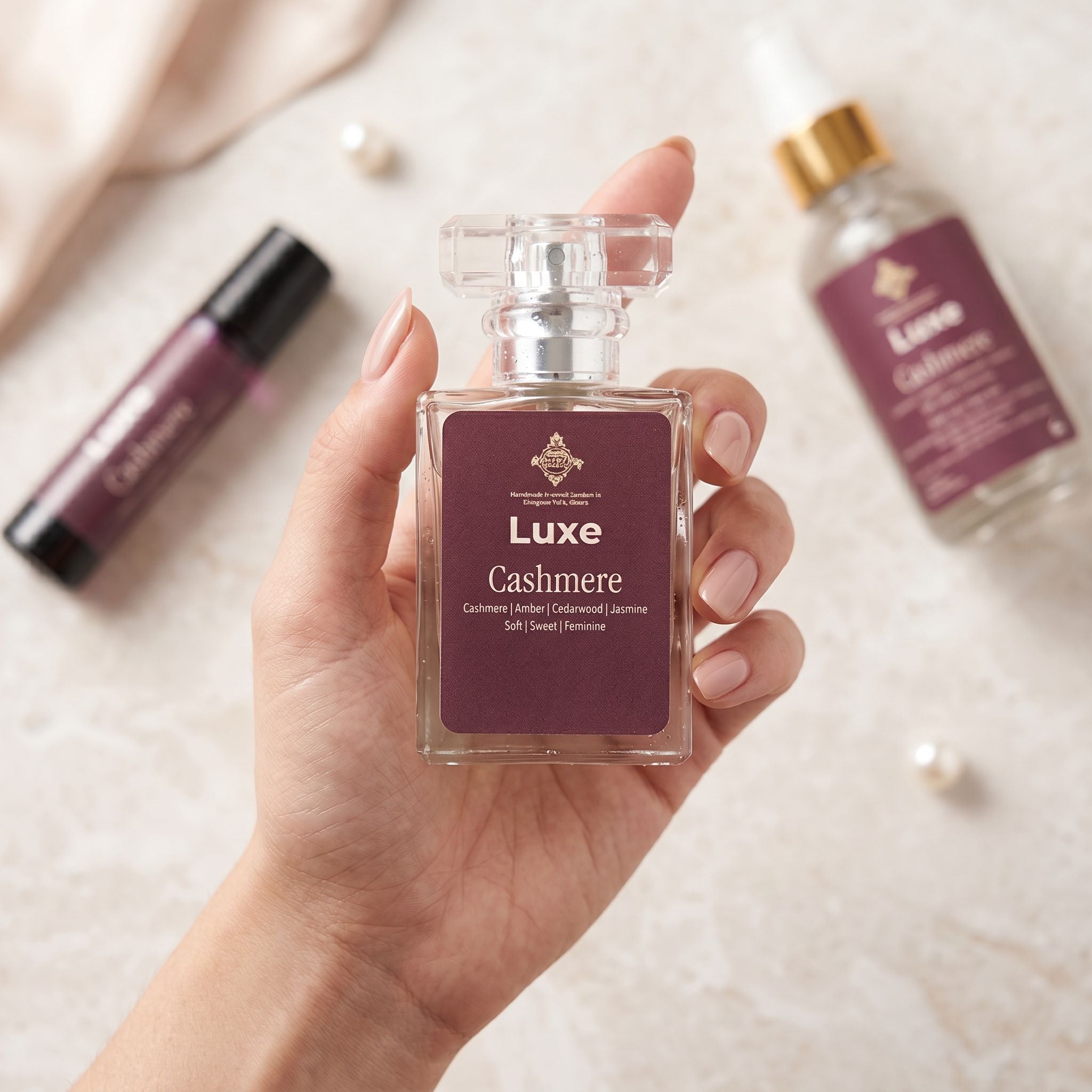 Hand holding a Luxe Cashmere perfume bottle with other perfume bottles in the background.