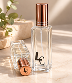 Two clear perfume bottles with bronze caps on a light wooden surface.