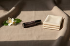 Black Luxe Cashmere roller with chocolate brown label on cream colored linen with cashmere and jasmine surrounding the roller for softness and warmth.