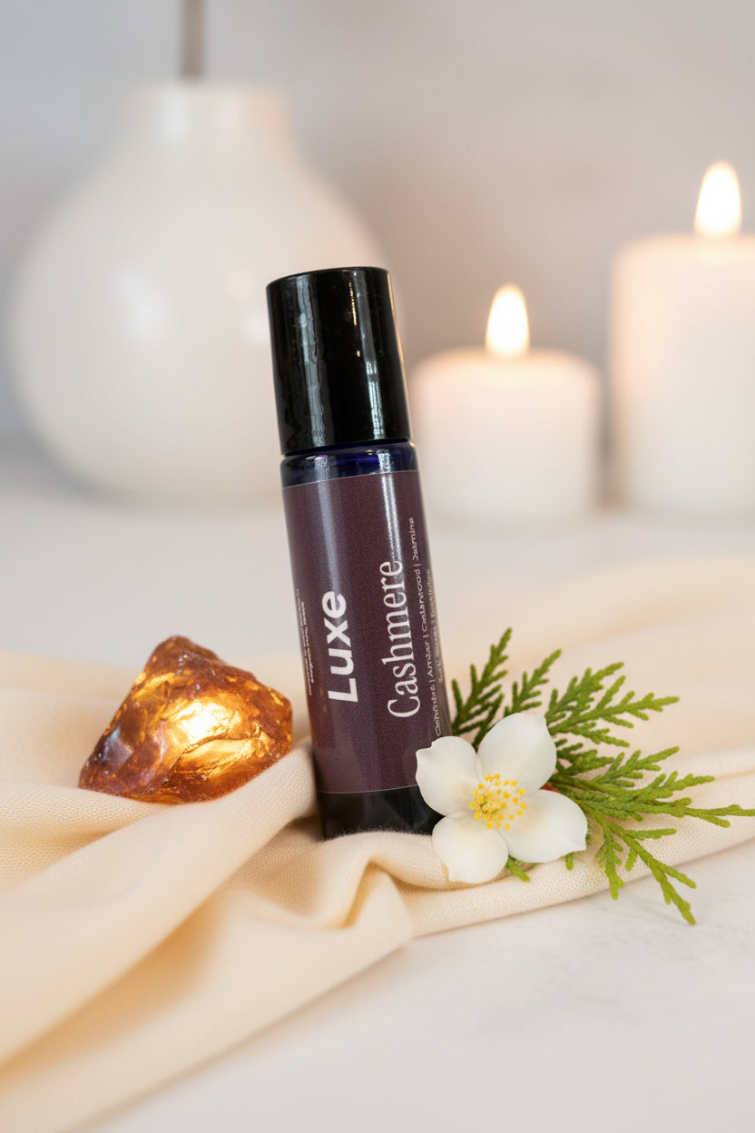 Luxe Cashmere perfume bottle on a taupe linen surface with amber and jasmine flowers with soothing candles in the background. 