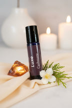 Luxe Cashmere perfume bottle on a taupe linen surface with amber and jasmine flowers with soothing candles in the background. 