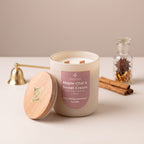 A 10oz beeswax candle in a frosted glass jar with a wooden lid leaning beside it on a tabletop. The front label reads 'Maple Chai & Sweet Cream' and shows the brand 'The Candle Company'.