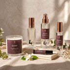 Blissfully Rooted Luxe Cashmere collection flat lay with candle, two eau de parfum spray bottles, a mist spray, and a rollerball, styled with linen, eucalyptus, and a jasmine flower