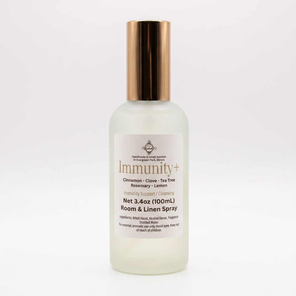 A frosted glass bottle of Immunity+ Room & Linen Spray with a metallic rose gold cap, shown on a clean white background.